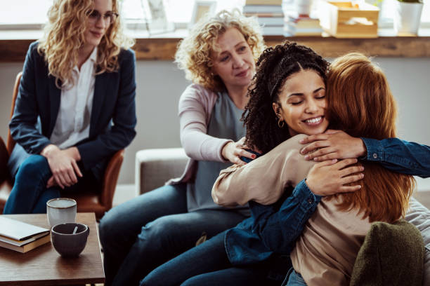 caring female counselor hugs a female patient during a group therapy session.